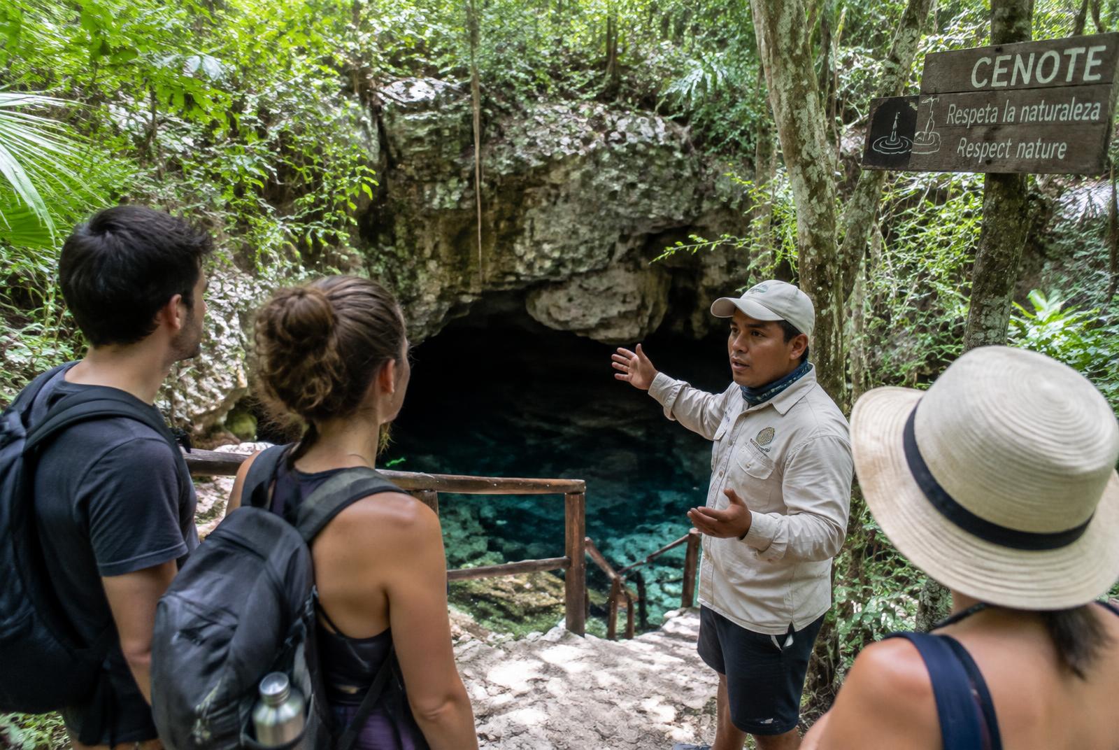 Guía y viajeros en la entrada de un cenote rodeado de selva